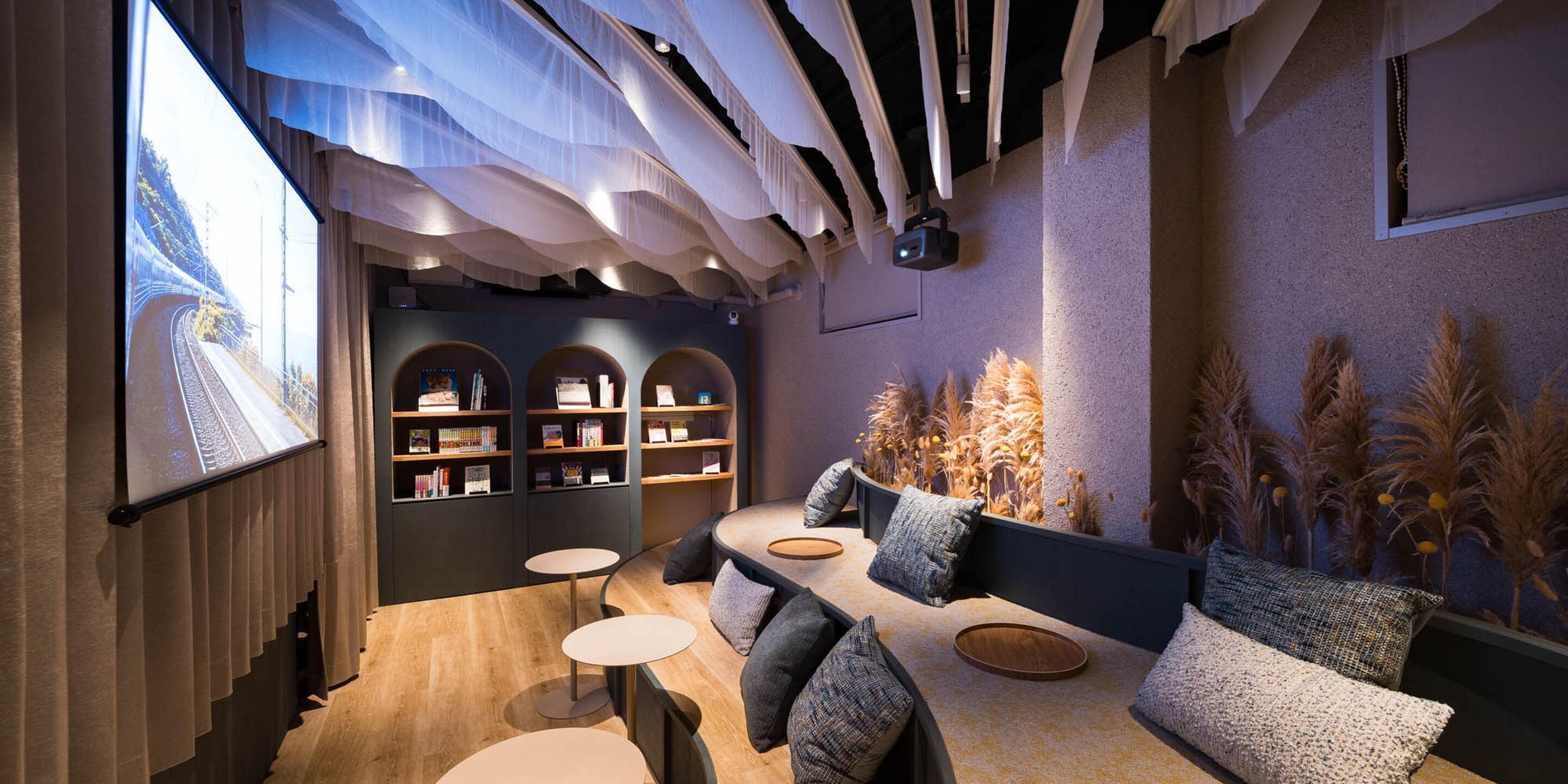A modern interior with a curved sofa, small round tables, and a bookshelf.
