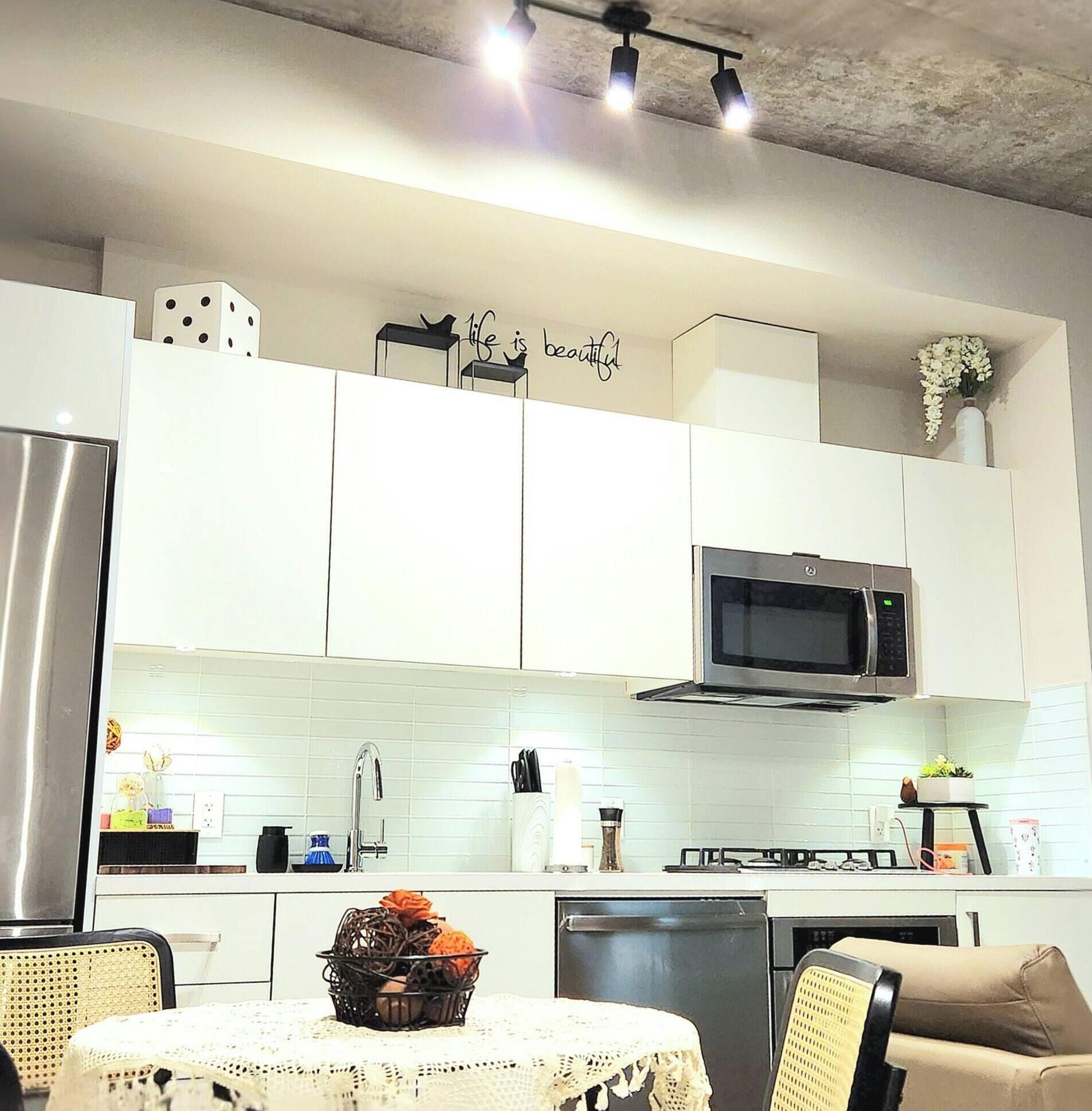 Una cocina moderna con armarios blancos, un microondas y un comedor con mesa y sillas.