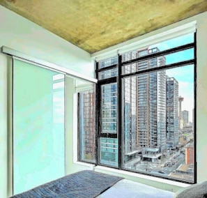 Una habitación con ventanas amplias, una cama y vistas a edificios altos.