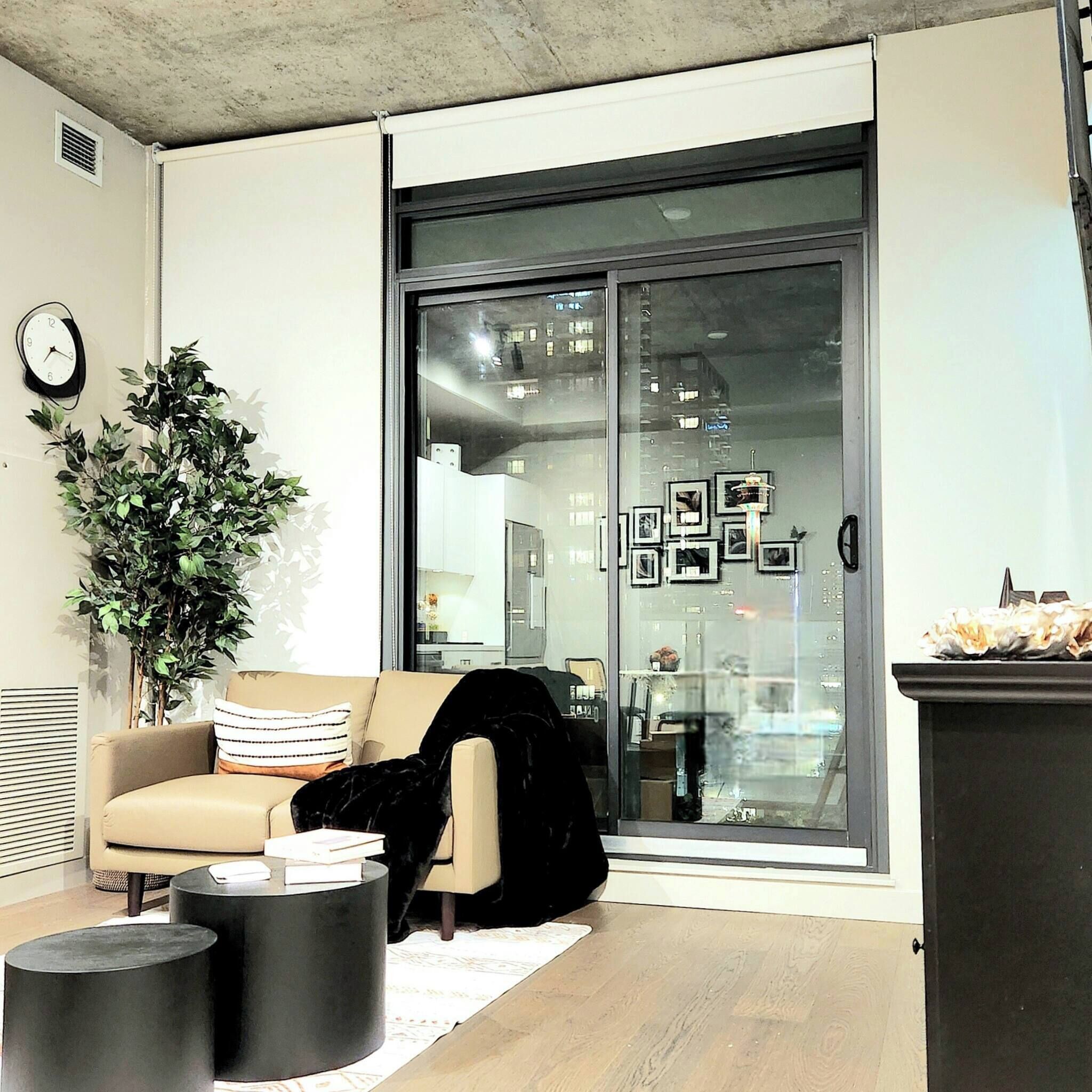 Ein modernes Wohnzimmer mit einer Couch, einem Blumentopf, einem runden Couchtisch und einer Glastür, die in einen Küchenbereich führt.