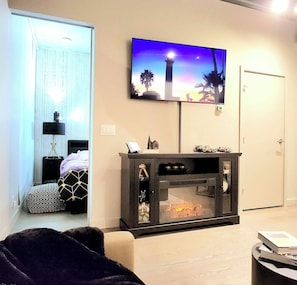 Una sala de estar moderna con chimenea, un televisor de pantalla plana montado arriba y una puerta a la derecha.