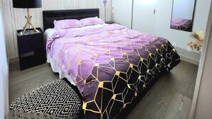Un dormitorio con cama, mesita de noche, lámpara, espejo y estante en la pared.