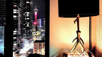 A bed with a view of a cityscape at night, including a tower with colorful lights.