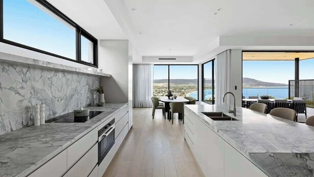 Eine moderne Küche mit Marmorarbeitsplatte, ein Essbereich mit Tisch und Stühlen sowie große Fenster mit Blick auf das Meer.