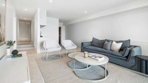 Ein modernes Wohnzimmer mit einem grauen Sofa, weißen Sesseln und einem Couchtisch.