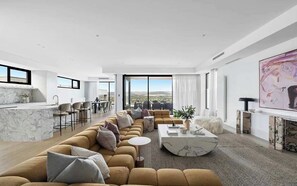 A modern living room with a sofa, coffee table, and a view of the outdoors. - Elèvè | Luxury in Mount Martha with Gas Heated Pool & Bay Views (Mount Martha)