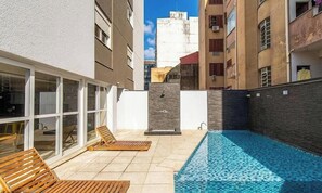 A rooftop pool area with sun loungers and a view of surrounding buildings. - Studio in Condo w/ Pool in POA Pue0308 (Porto Alegre)