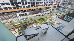 Ein Balkon mit Korbstuhl, Tisch und Blick auf eine Straße mit Autos und Grün.
