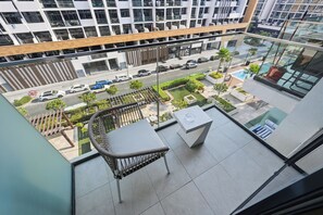 A balcony with a wicker chair, a small table, and a view of a street with cars and greenery below. - Bloomfields Studio in Azizi Riviera 34 (Dubai)