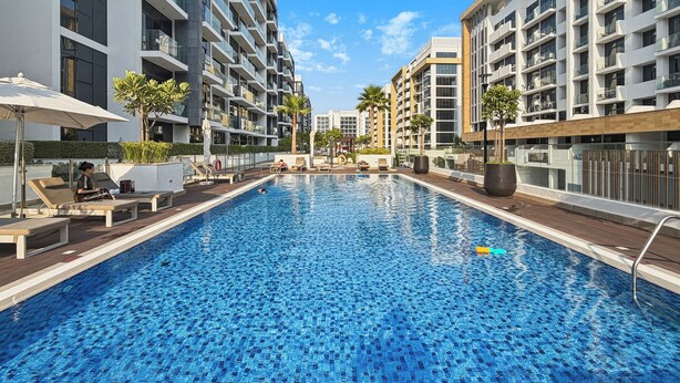 Ein Schwimmbecken mit Liegestühlen und Sonnenschirmen, umgeben von modernen Gebäuden.