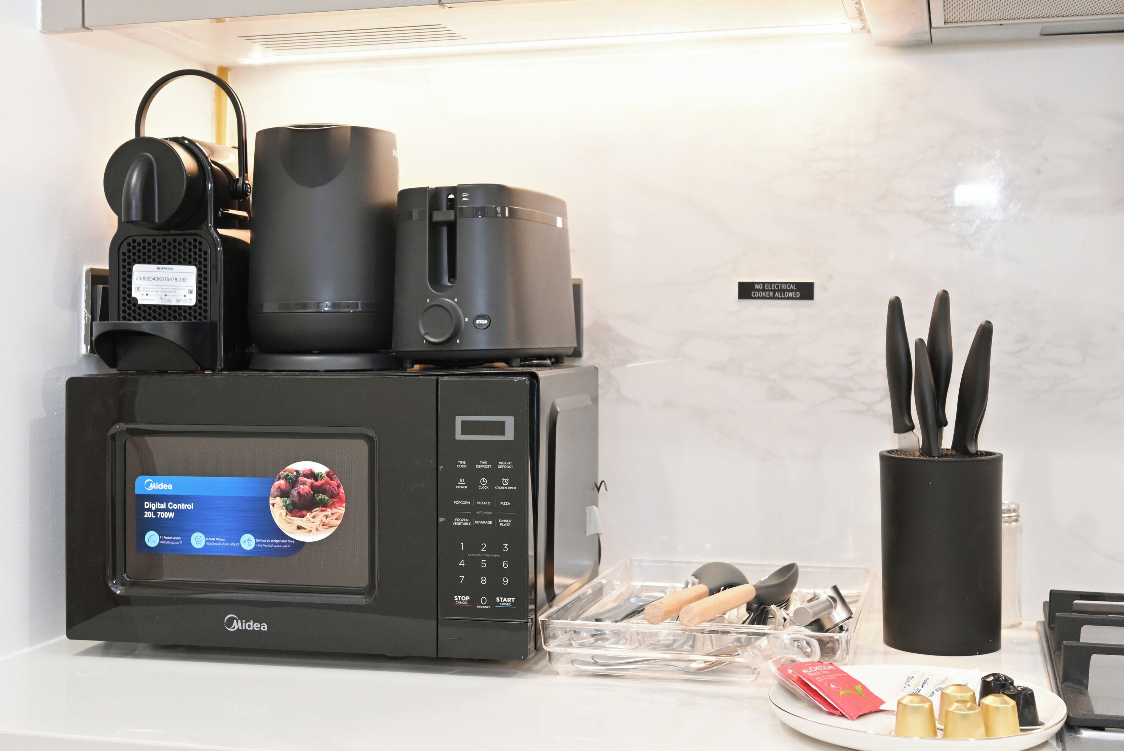 Une cuisine équipée d’un panneau de commande numérique, d’un four à micro-ondes, d’une bouilloire et d’un porte-couteaux.