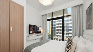Ein modernes Hotelzimmer mit einem großen Bett, einem Kleiderschrank, einem Wand-TV und einem Balkon mit Stadtblick.