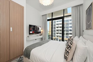 A modern hotel room with a large bed, a wardrobe, a mounted TV, and a balcony with a view of the city. - Bloomfields Studio in Azizi Riviera 34 (Dubai)