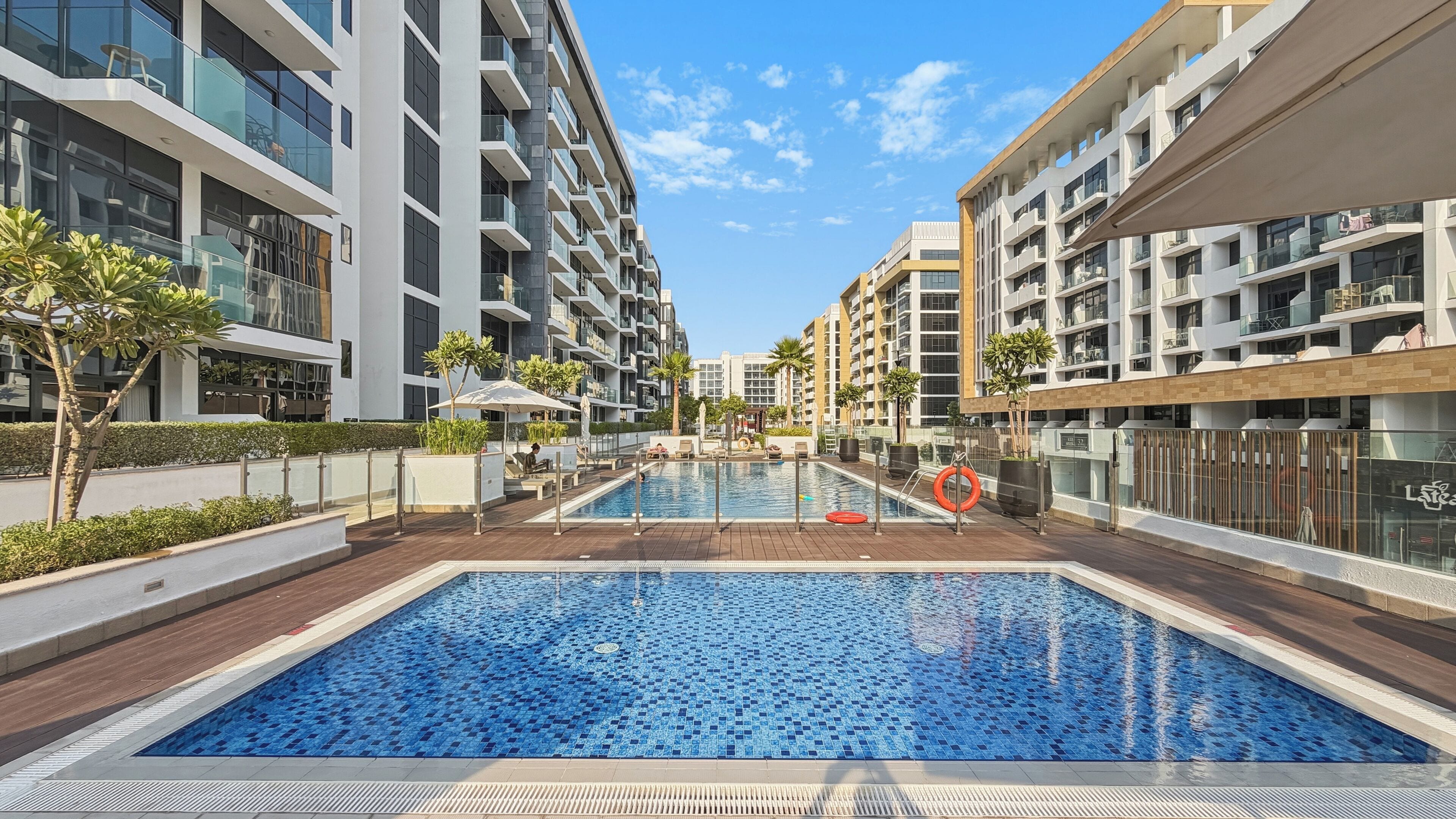 Un immeuble résidentiel moderne doté d’une piscine centrale, entouré de balcons et surplombant un ciel dégagé.