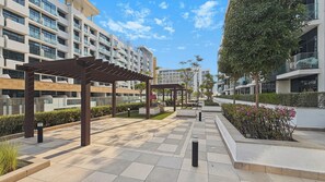 A modern outdoor area with a pergola, seating, and a pathway leading to a building with balconies. - Bloomfields Studio in Azizi Riviera 34 (Dubai)