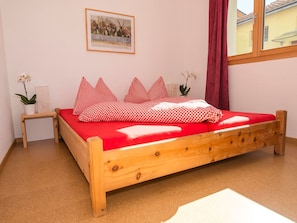 A single-bed room with a wooden frame, red bedding, and a small bedside table with a plant. - Chasa Berry, (Ftan) by Interhome (Ftan)