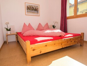 A single-bed room with a red bedspread, wooden headboard, and a small bedside table with a plant. - Chasa Berry, (Ftan) by Interhome (Ftan)