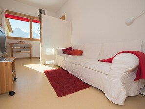 A white sofa with red cushions, a red rug, a wooden side table with a basket, and a television on a stand. - Chasa Berry, (Ftan) by Interhome (Ftan)