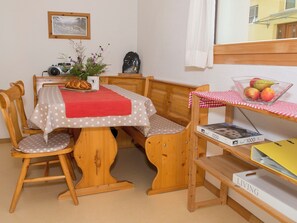 A cozy room with a wooden table, chairs, a small shelf with a bowl of fruit, a clock, and a framed picture on the wall. - Chasa Berry, (Ftan) by Interhome (Ftan)