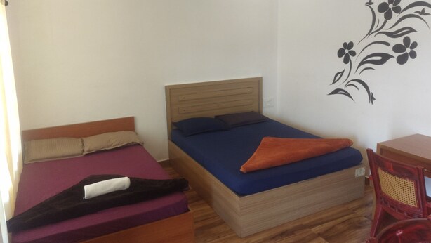 A small, single-room accommodation with two beds, a wooden headboard, a wall decoration, and a small table. - Vagadrops (Peermade)