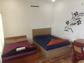 A small, single-room accommodation with two beds, a wooden headboard, a wall decoration, and a small table. - Vagadrops (Peermade)