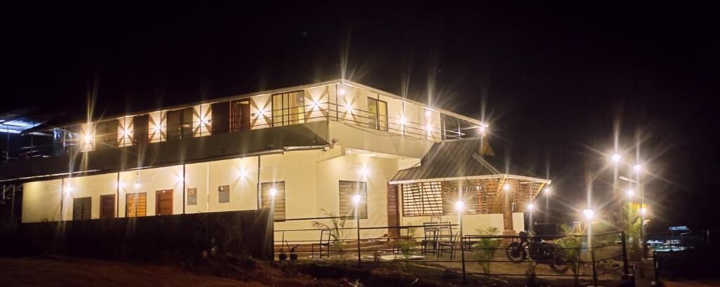 Un edificio de dos pisos con un balcón y un espacio cubierto, iluminado por luces exteriores.