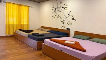 Una habitación con dos camas, piso de madera, cortina amarilla y un mural en la pared.