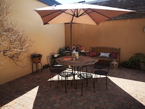 Eine Terrasse im Freien mit einem runden Holztisch, vier Stühlen, einer Bank und einem großen Sonnenschirm.
