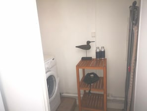A laundry area with a washing machine, a wooden shelf with bottles, and a bird-shaped light fixture. - La Parenthèse d'Honfleur ~ 4 Bedrooms & Private Courtyard (La Rivière-Saint-Sauveur)