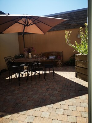 Un patio con una mesa y sillas, un banco de madera, una sombrilla grande y una jardinera con flores.
