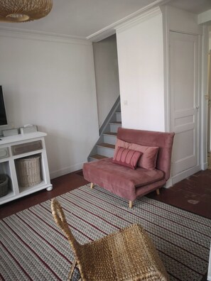 Ein Wohnzimmer mit einem rosafarbenen Sofa, einem Korbstuhl, einer weißen Unterhaltungseinheit und einer Treppe.