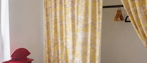 A room with a wooden bed, a red desk, a clear chair, a wicker basket, and yellow patterned curtains.