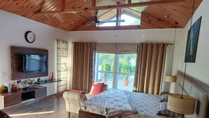 A bedroom with a bed, a TV, a desk, and a window with curtains.