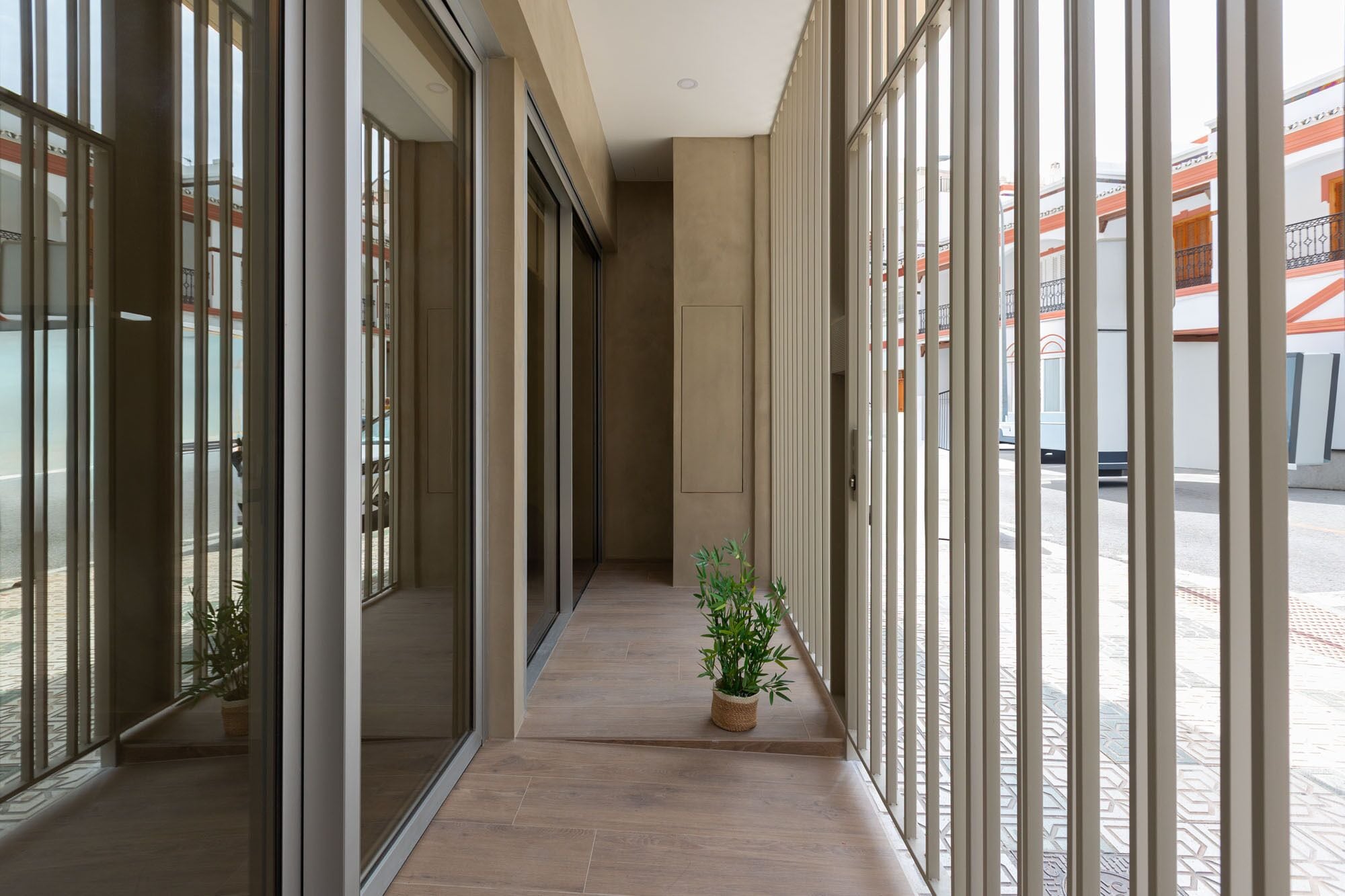 Un couloir avec des portes et des fenêtres en verre, une plante en pot et un sol carrelé.