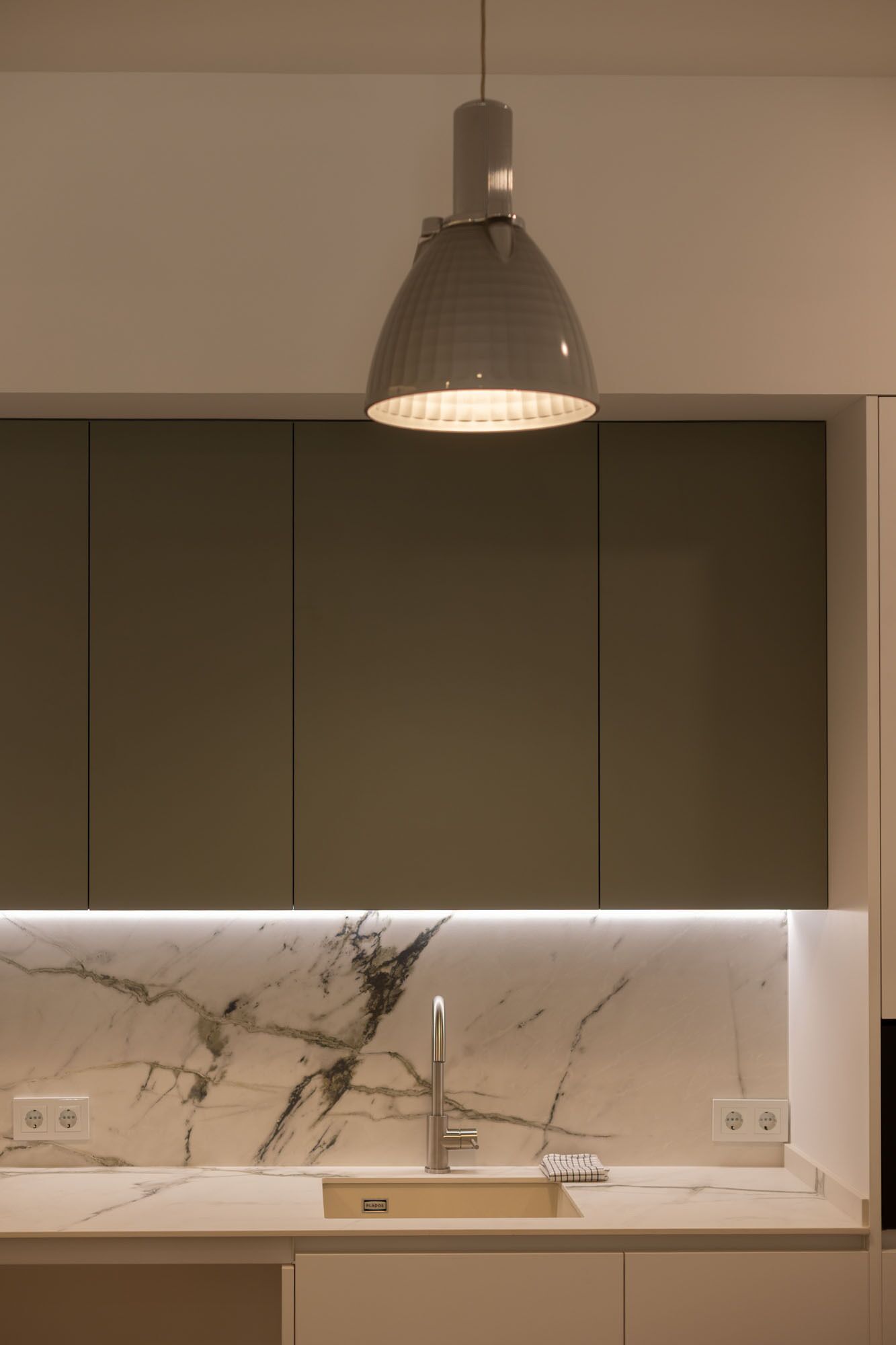 A modern kitchen with a marble countertop, a single faucet, and a pendant light above the sink.