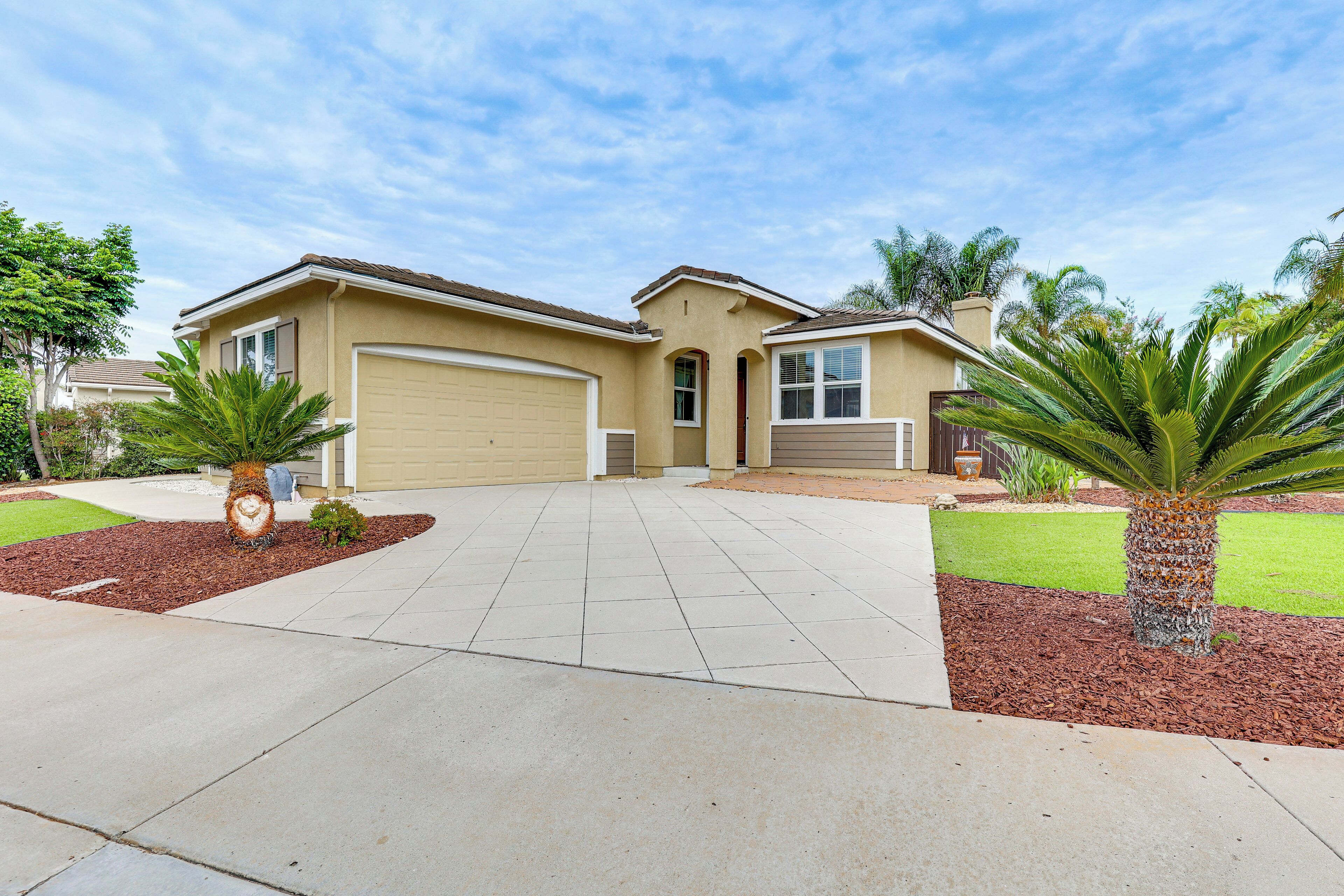 A residential house with a garage, a driveway, and landscaped garden with palm trees.