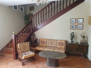 Een trap met houten balustrades, een houten bank met gestreepte kussens, een ronde tafel en een beeld op een kast.