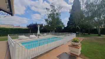 A rectangular outdoor swimming pool with a white fence, a white umbrella, and a planter with flowers.