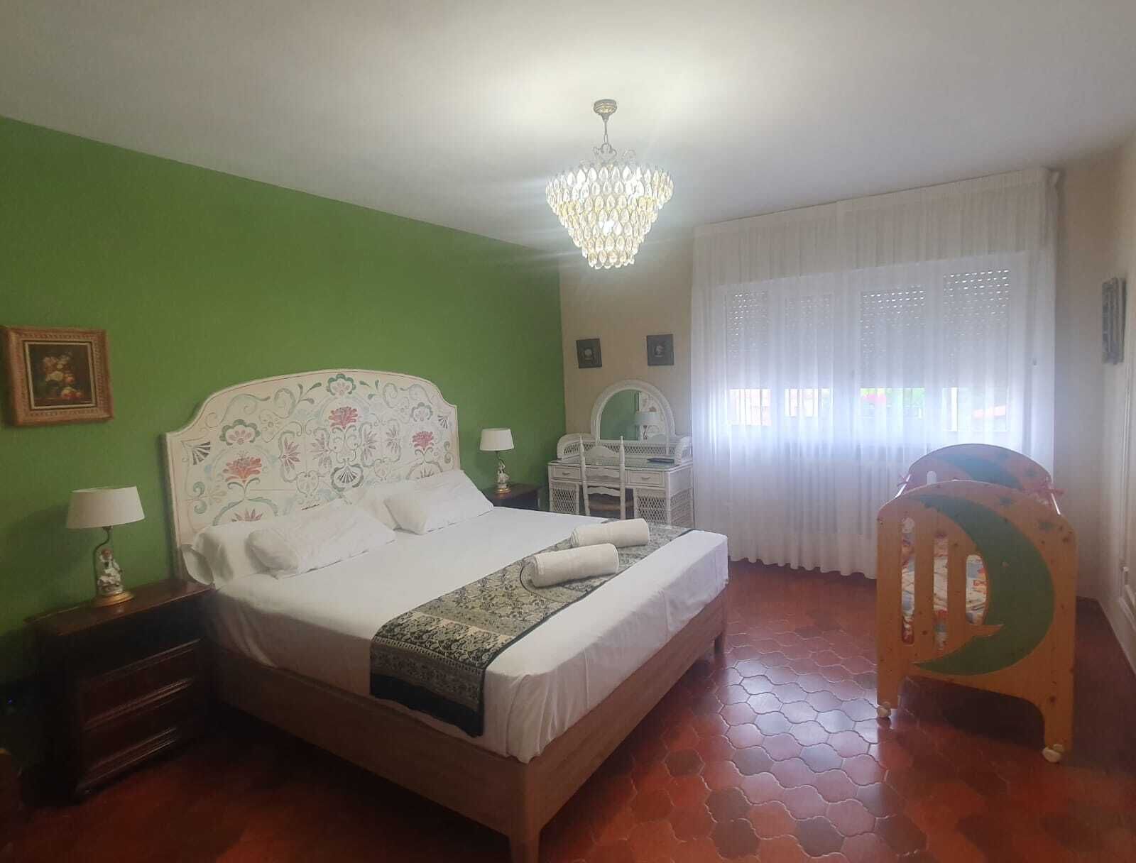 A bedroom with a bed, a dresser, a chair, a vanity, and a chandelier.