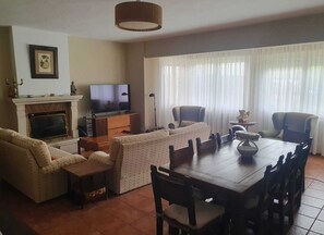 Een woonkamer met een open haard, televisie, bank, eettafel en stoelen.