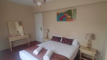 A bedroom with a large bed, two bedside tables, a chandelier, a painting, and a mirror.