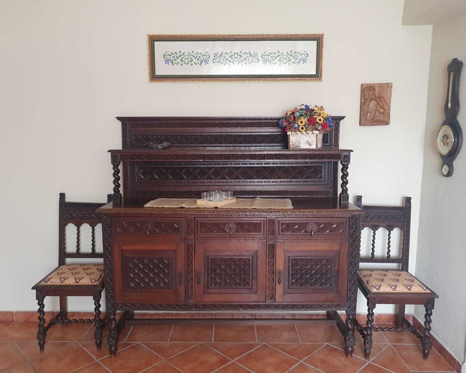 Un banco de piano de madera con un arreglo floral encima, una obra de arte enmarcada arriba y un reloj montado en la pared.