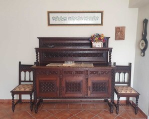 Een houten pianobank met een bloemstuk erop, een lijstwerk erboven en een wandklok.