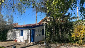 Un edificio blanco con detalles azules y techo de tejas, rodeado de vegetación y un cielo despejado.