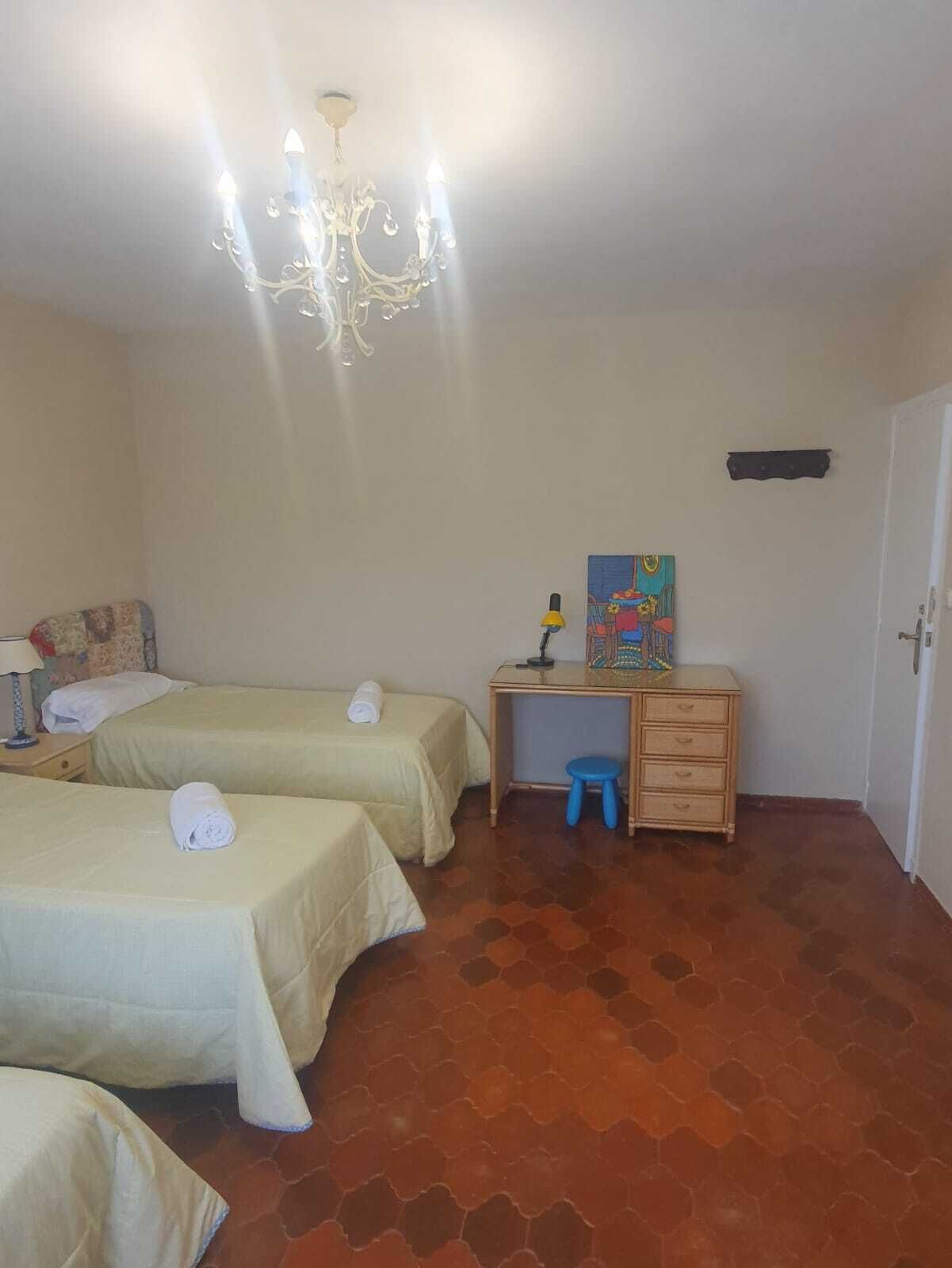 Een kamer met twee bedden, een bureau met stoel, een klein krukje, een schilderij en een kroonluchter.