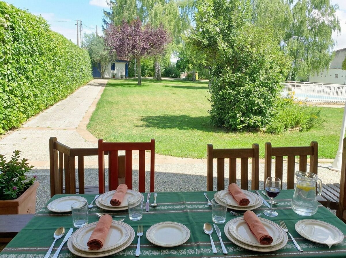 Mesa de comedor al aire libre con sillas, platos, cubiertos y una jarrón de agua.