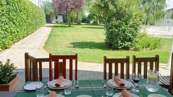 Mesa de comedor al aire libre con sillas, platos, cubiertos y una jarrón de agua.