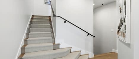 A staircase with carpeted steps and a black handrail, leading to a landing with a framed picture.