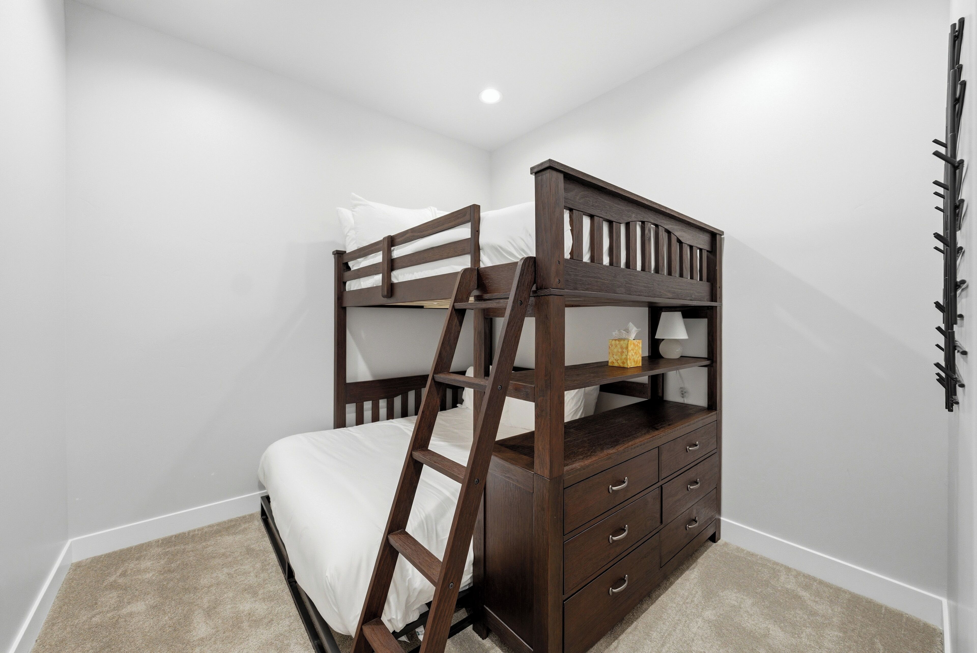Una cama litera con escalera, una mesita de noche con lámpara y un perchero en la pared.