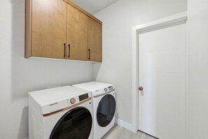 Ein Waschraum mit zwei weißen Samsung Waschmaschinen, Holzausbau und einer weißen Tür.